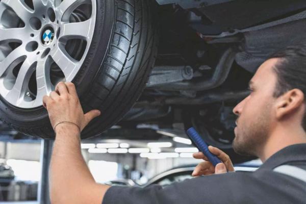 Ein Mitarbeiter in einer BMW Werkstatt prüft das Profil des linken Hinterreifens eines BMW.