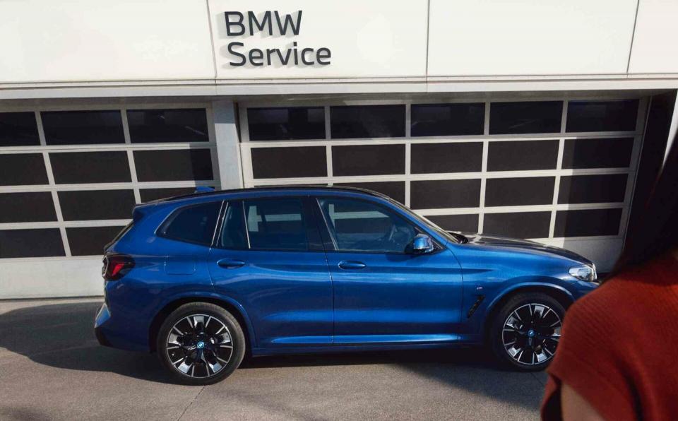 Ein blauer BMW iX3 M steht vor dem Tor einer BMW Service Werkstatt.